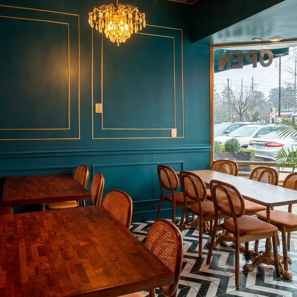 Restaurant interior with teal walls, gold trim, chandeliers, wooden tables, and orange booth seating.